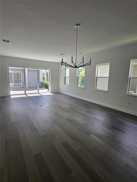 A spacious, empty room features dark wood-look flooring, a modern chandelier, and sliding glass doors — 10172 PEARSON AVENUE, ORLANDO, FL