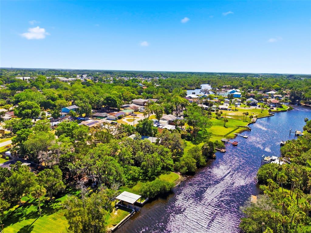 An aerial view shows a river winding through a lush, tree-filled residential neighborhood — 5651 MONROE STREET, NEW PORT RICHEY, FL