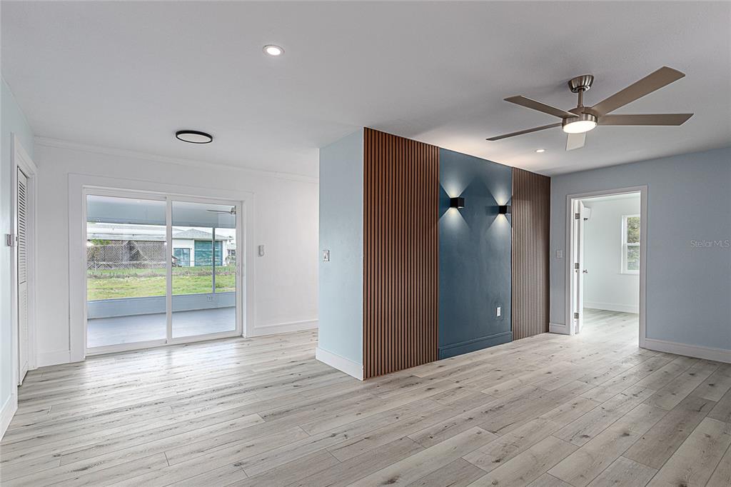 A living room features light wood-look flooring, a blue accent wall with wood slats, and sliding doors — 3208 PINETREE STREET, PORT CHARLOTTE, FL
