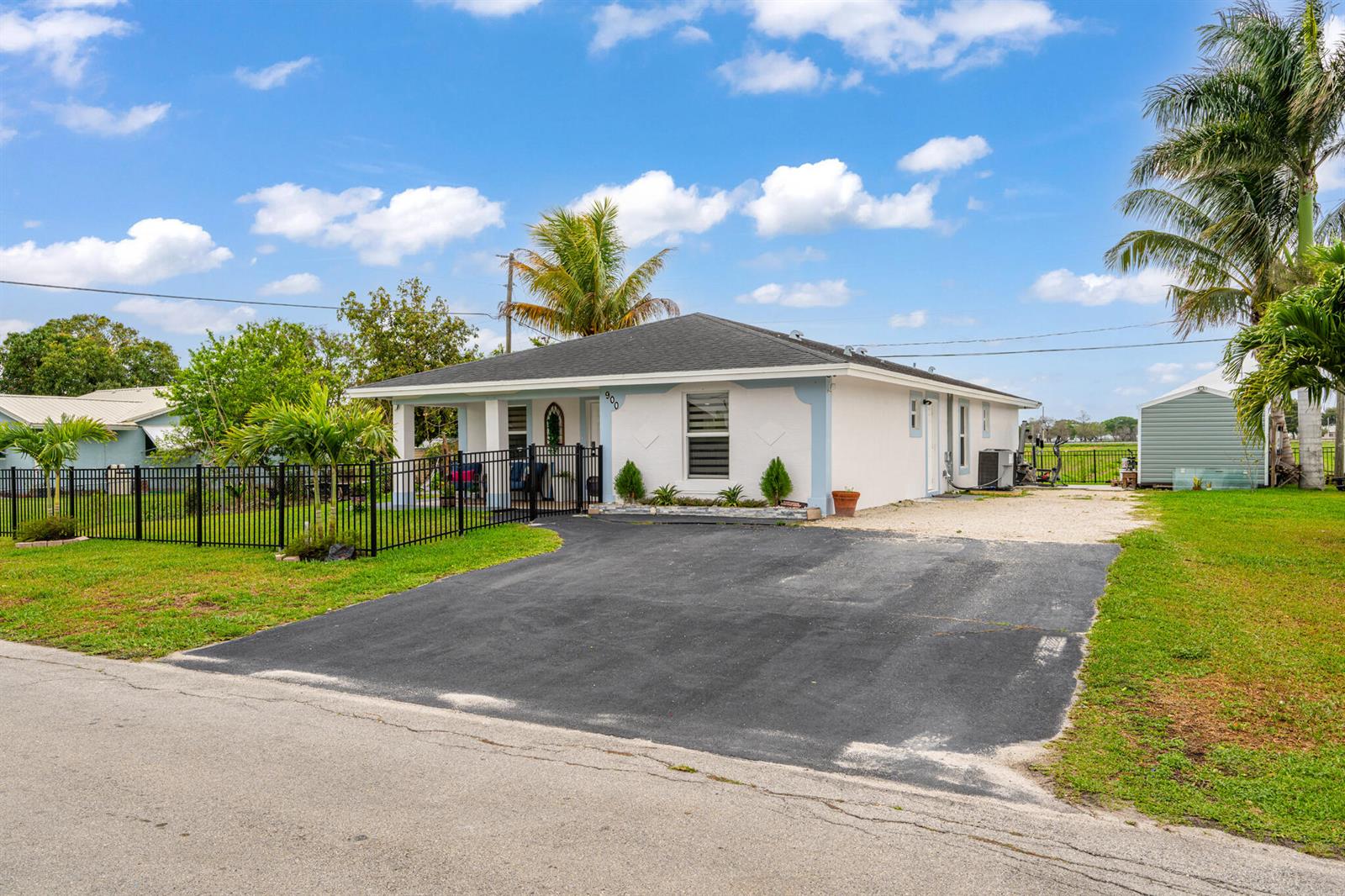A white, single-story house with a black metal fence and a paved driveway — 900 SW 12th Street, Belle Glade FL 33430, BELLE GLADE, FL