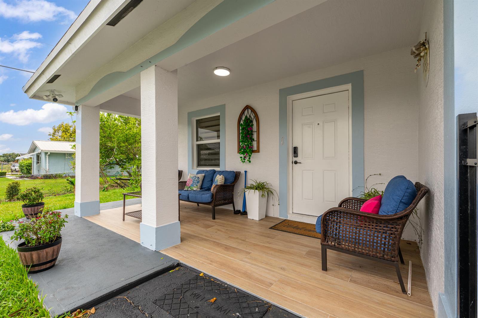 A covered front porch features wood-look tile flooring, wicker furniture, and a white front door — 900 SW 12th Street, Belle Glade FL 33430, BELLE GLADE, FL