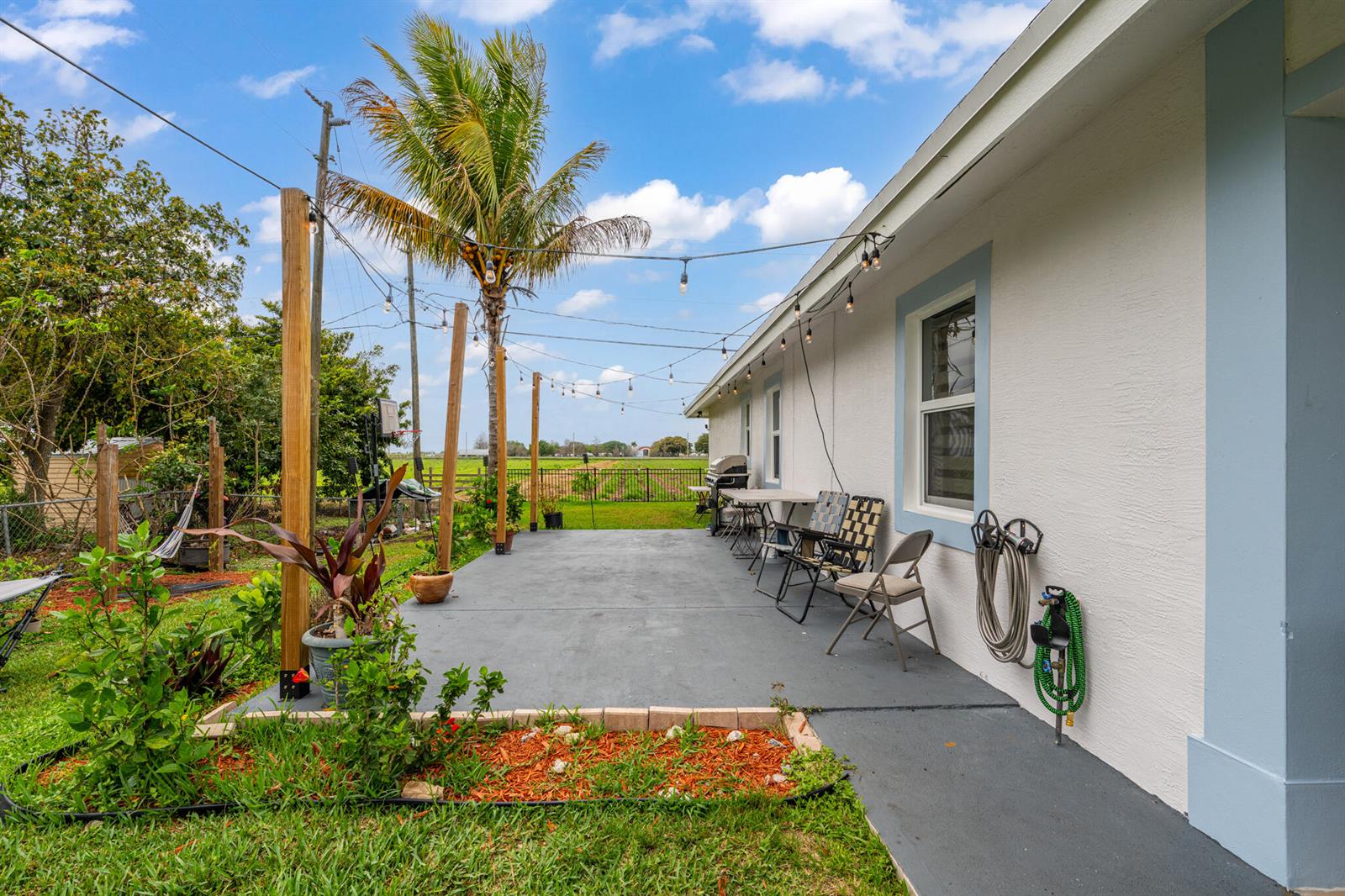 A concrete patio with string lights extends along the side of a white house — 900 SW 12th Street, Belle Glade FL 33430, BELLE GLADE, FL
