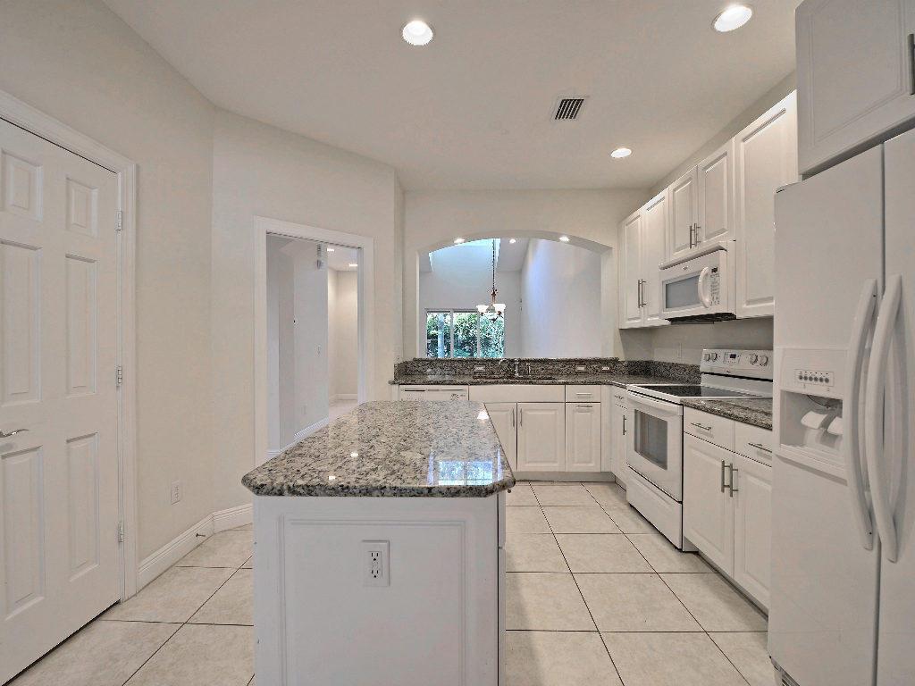 A kitchen with white cabinets, granite countertops, a center island, and tile flooring — 1645 Baseline Lane, Vero Beach FL 32967, VERO BEACH, FL