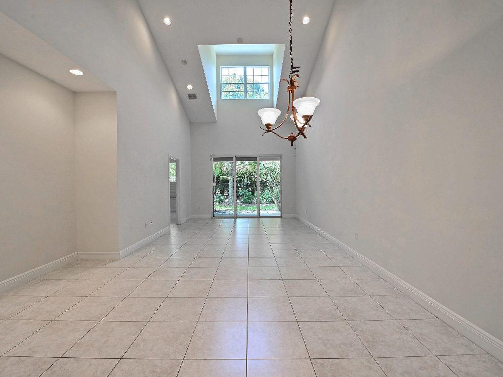 A bright, empty room features high vaulted ceilings, tile flooring, and a large chandelier — 1645 Baseline Lane, Vero Beach FL 32967, VERO BEACH, FL