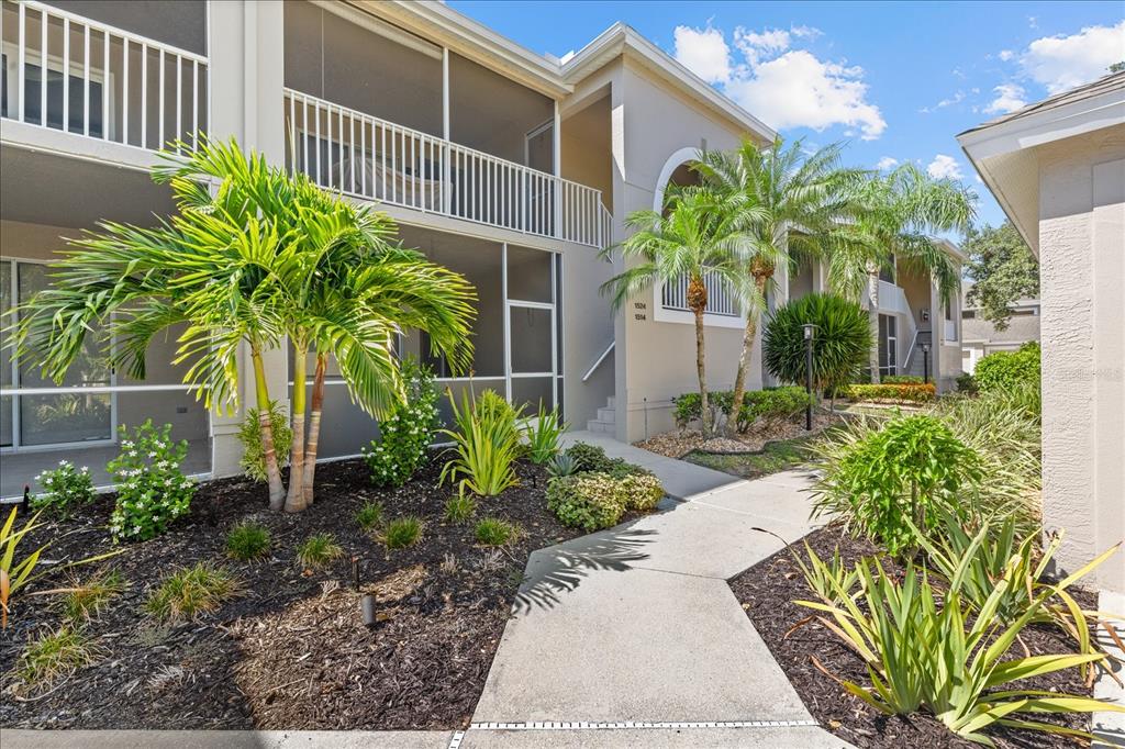 A concrete walkway leads to the entrance of a two-story apartment building with screened balconies — 9550 HIGH GATE DRIVE UNIT 1525, SARASOTA, FL