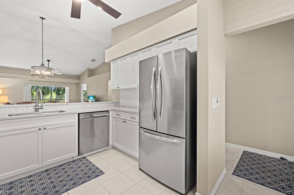 A kitchen features white cabinetry, stainless steel appliances, and a view into the living area — 9550 HIGH GATE DRIVE UNIT 1525, SARASOTA, FL