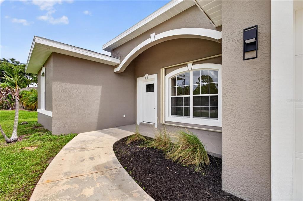A beige house exterior features a curved entryway arch, a white front door, and landscaping — 1146 WOODCREST LANE, NORTH PORT, FL