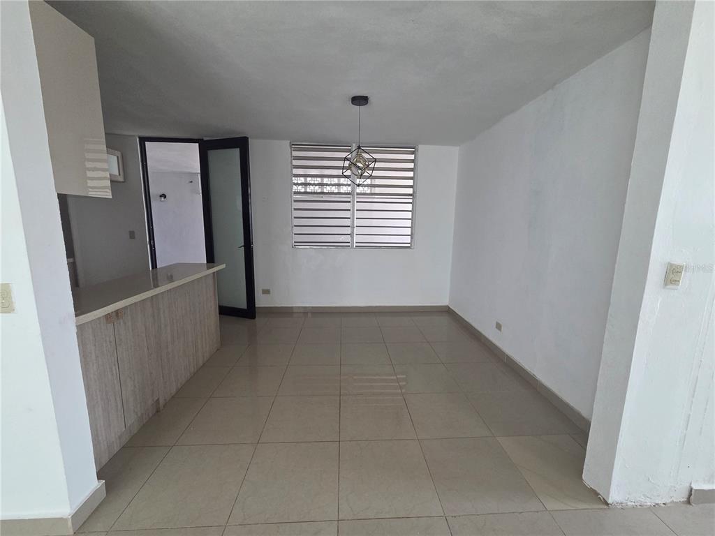 An empty room features light-colored tile flooring, a kitchen counter, and a modern pendant light — 24 calle 35 VILLA CAROLINA, CAROLINA, PR