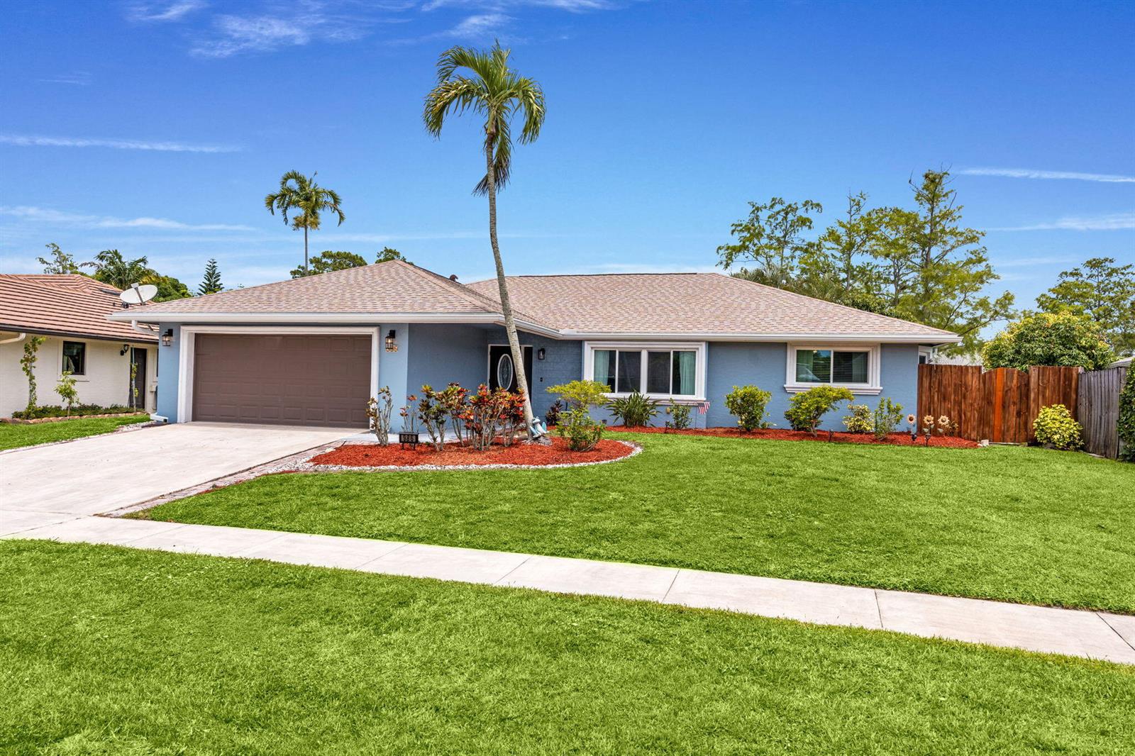 A blue single-story house with a brown garage door, a palm tree, and a lawn — 986 Cherry Lane, Wellington FL 33414, WELLINGTON, FL
