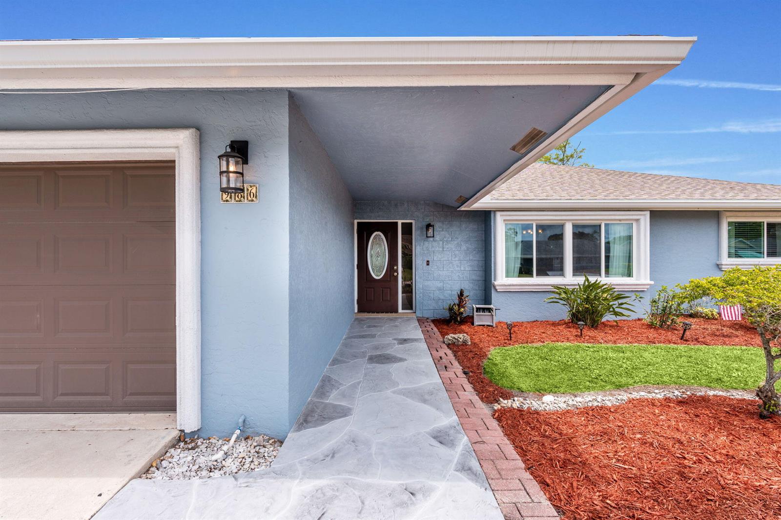 A light blue house exterior features a stone walkway leading to a dark brown front door — 986 Cherry Lane, Wellington FL 33414, WELLINGTON, FL