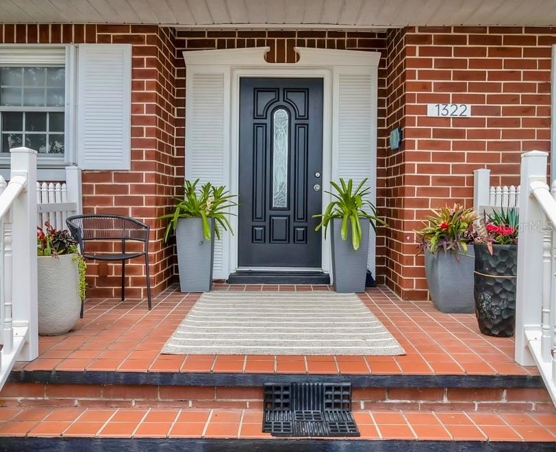 A brick front porch features a dark door, potted plants, a chair, and a rug — 1322 RIVERSIDE DRIVE, TITUSVILLE, FL