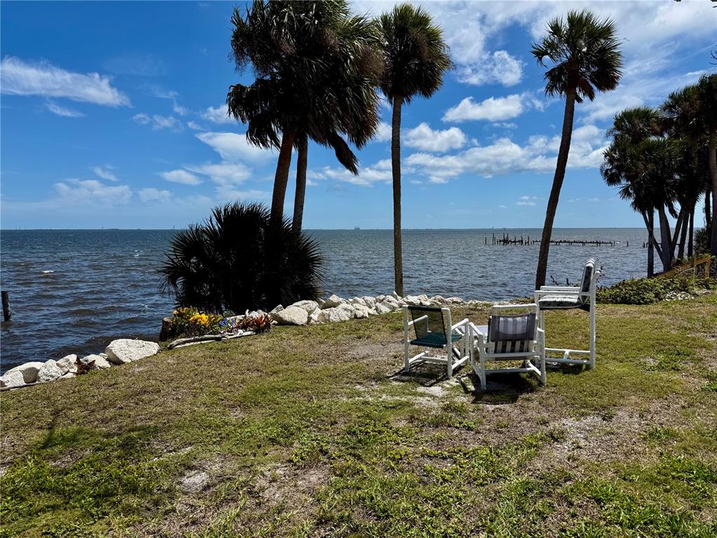 A grassy yard with outdoor chairs overlooks a body of water with palm trees — 1322 RIVERSIDE DRIVE, TITUSVILLE, FL