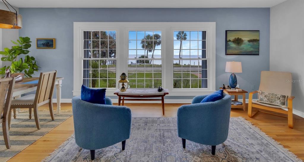 A living room with blue walls, two blue armchairs, and large windows overlooking the water — 1322 RIVERSIDE DRIVE, TITUSVILLE, FL