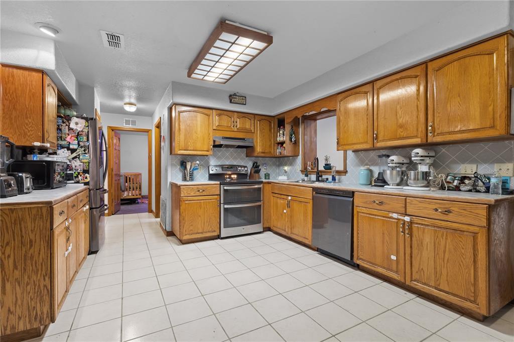 A kitchen with oak cabinets, stainless steel appliances, white tile flooring, and a drop ceiling light — 11235 SW 131ST TERRACE, DUNNELLON, FL