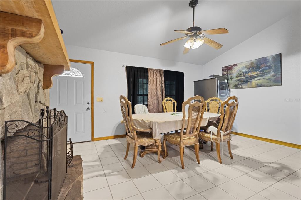 A dining room features a stone fireplace, tiled floors, a wooden table, and a ceiling fan — 11235 SW 131ST TERRACE, DUNNELLON, FL