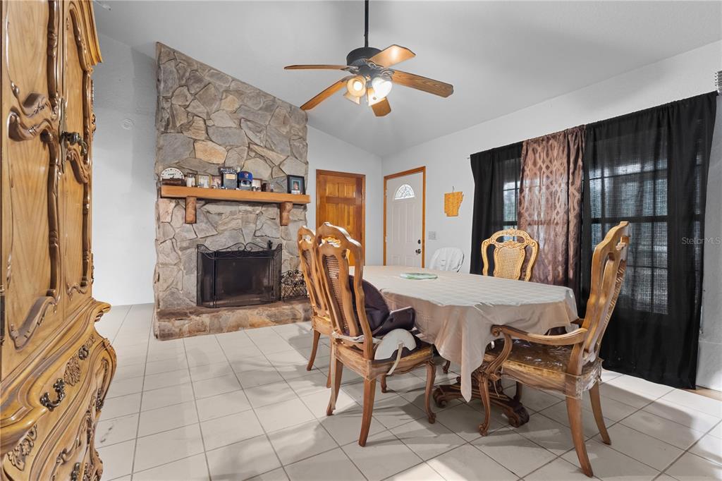 A dining room features a stone fireplace, tile flooring, a ceiling fan, and wooden furniture — 11235 SW 131ST TERRACE, DUNNELLON, FL