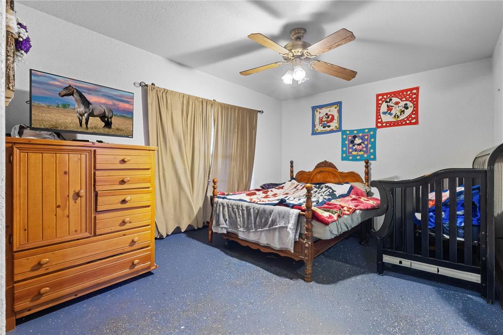 A bedroom features a wooden dresser, a bed with a patterned quilt, and a black crib — 11235 SW 131ST TERRACE, DUNNELLON, FL