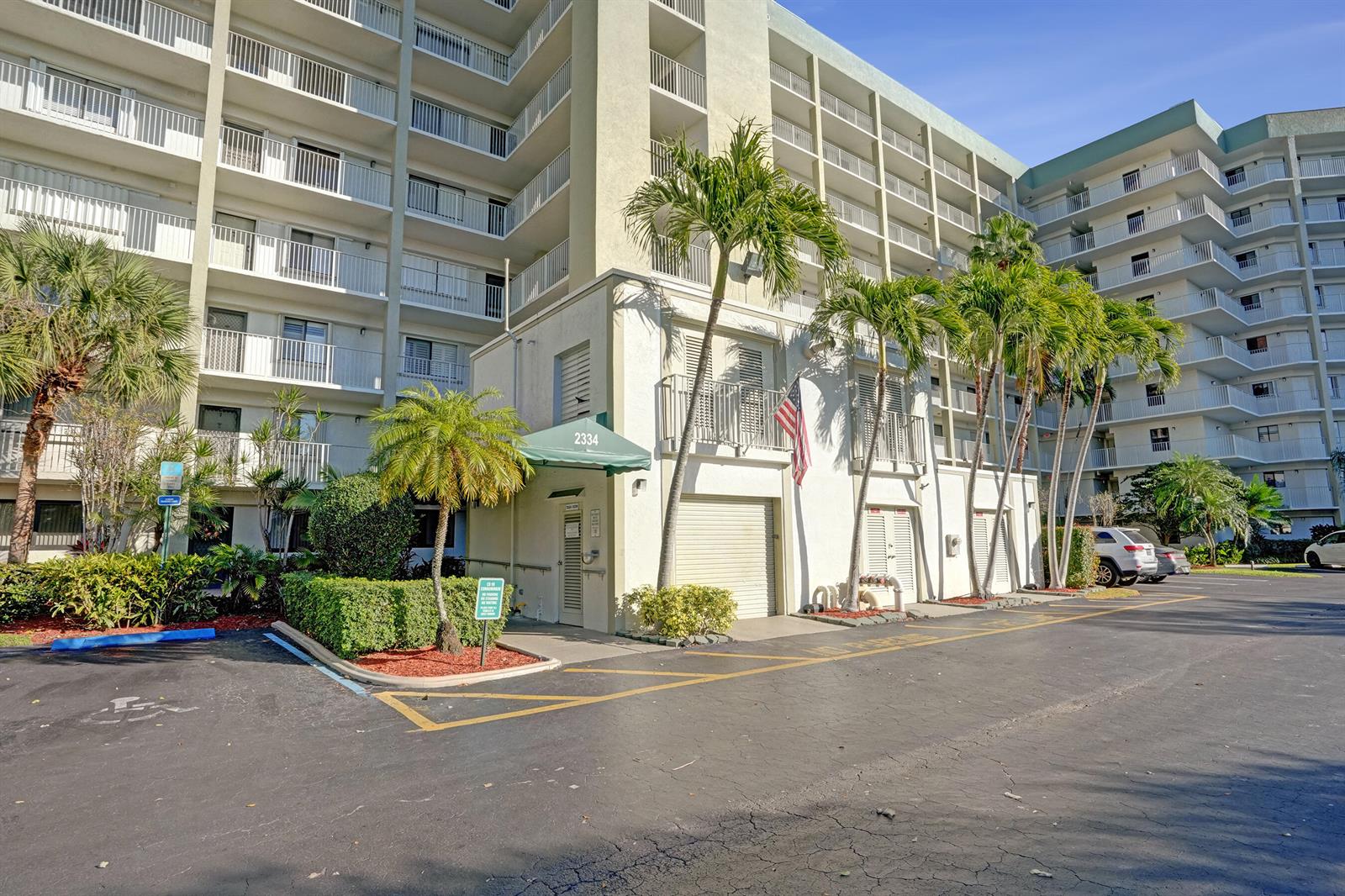 The exterior of a multi-story apartment building features a green awning over a ground-level entrance — 2334 S Cypress Bend Drive # 907, Pompano Beach FL 33069, POMPANO BEACH, FL