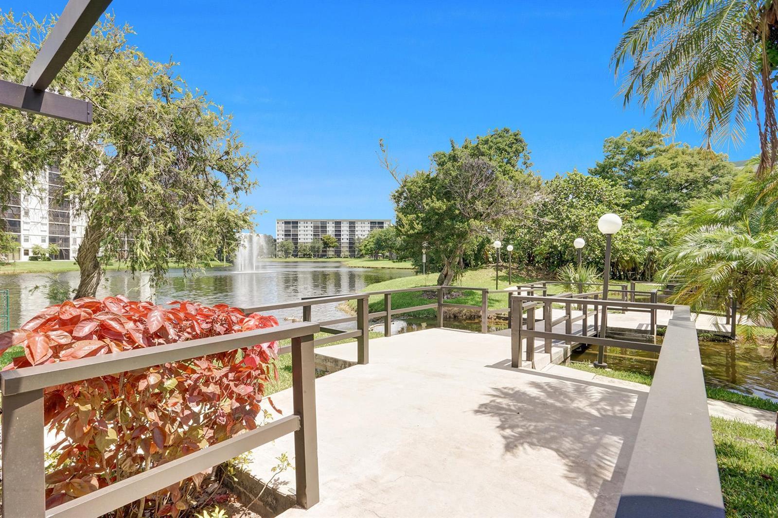 A concrete deck with railings overlooks a pond with a fountain and surrounding apartment buildings — 2334 S Cypress Bend Drive # 907, Pompano Beach FL 33069, POMPANO BEACH, FL
