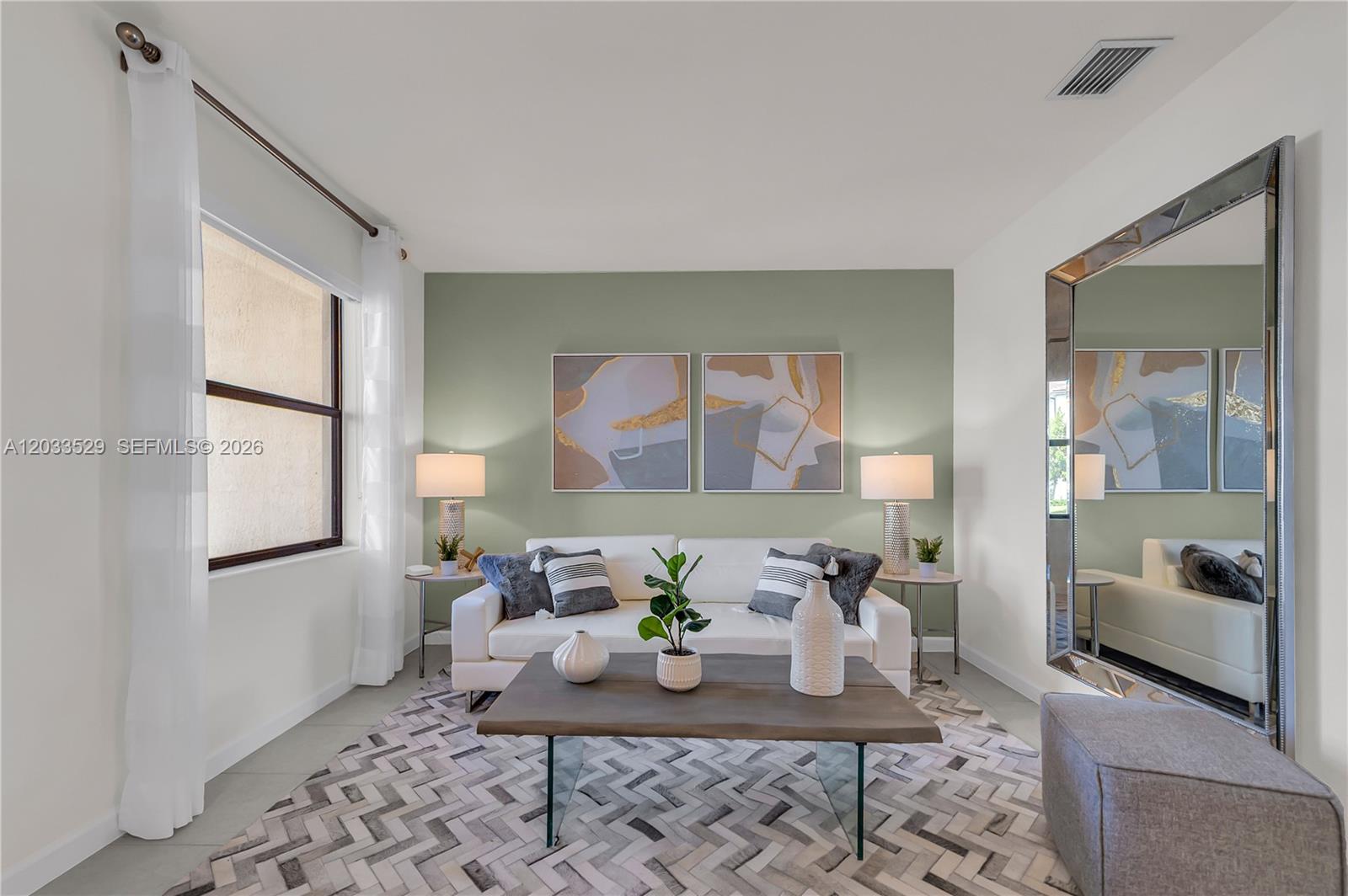 A living room features a sage green accent wall, white sofa, and a large floor mirror — 12980 SW 233rd Ter, Homestead FL 33032, HOMESTEAD, FL