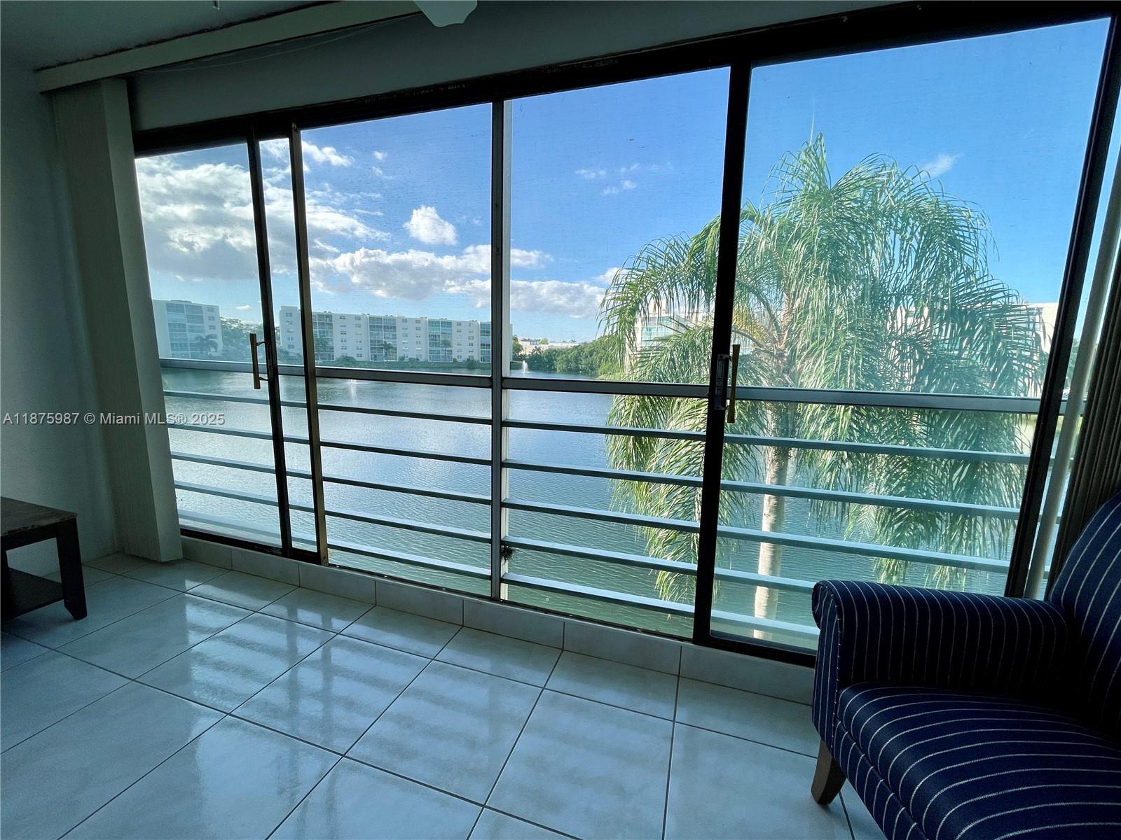 A sunroom with tiled floors features large sliding glass doors overlooking a lake and palm tree — 131 SE 3rd Ave # 305, Dania Beach FL 33004, DANIA BEACH, FL