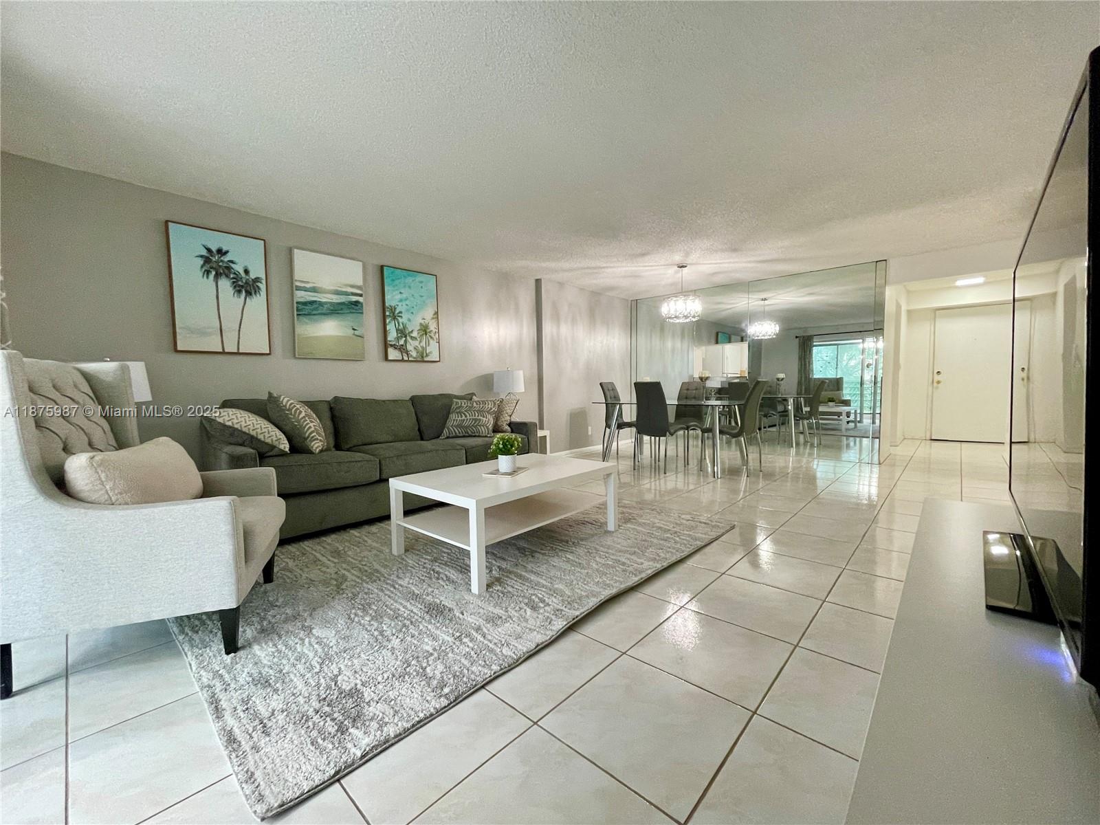 A living and dining area features tile floors, a gray sofa, and a mirrored wall — 131 SE 3rd Ave # 305, Dania Beach FL 33004, DANIA BEACH, FL
