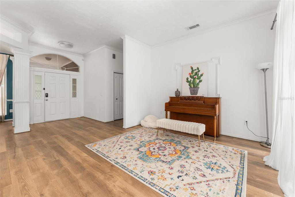 A living room features wood-look flooring, a piano, a patterned area rug, and an entryway — 11520 NW 8TH LANE, GAINESVILLE, FL