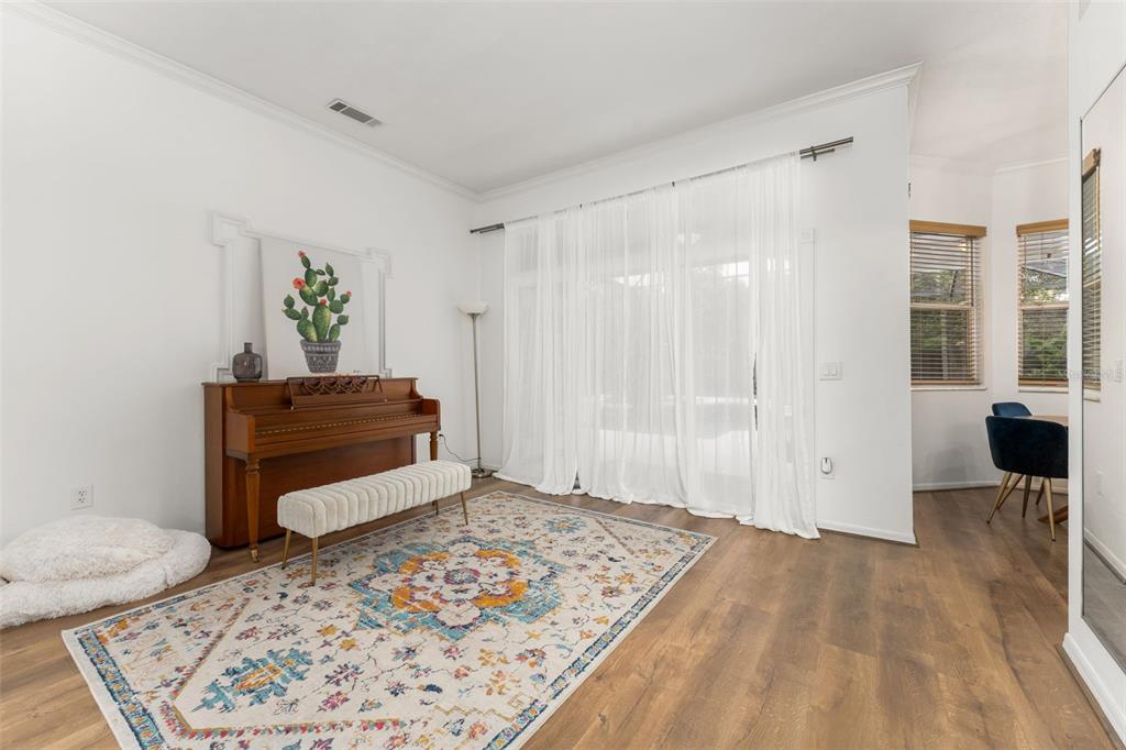 A living room features a piano, a patterned rug, and sheer curtains over sliding glass doors — 11520 NW 8TH LANE, GAINESVILLE, FL