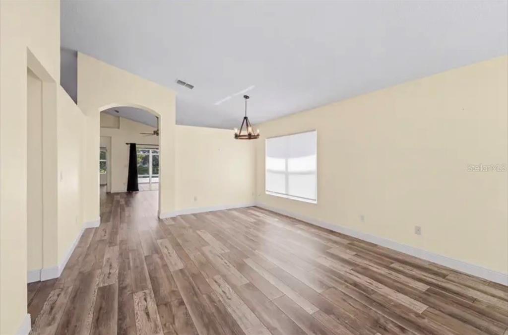 An empty room with light-colored walls, wood-look flooring, a vaulted ceiling, and a chandelier — 2782 JOSEPH CIRCLE, OVIEDO, FL