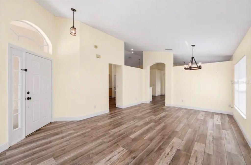 An empty living room features light yellow walls, wood-look flooring, and a vaulted ceiling — 2782 JOSEPH CIRCLE, OVIEDO, FL