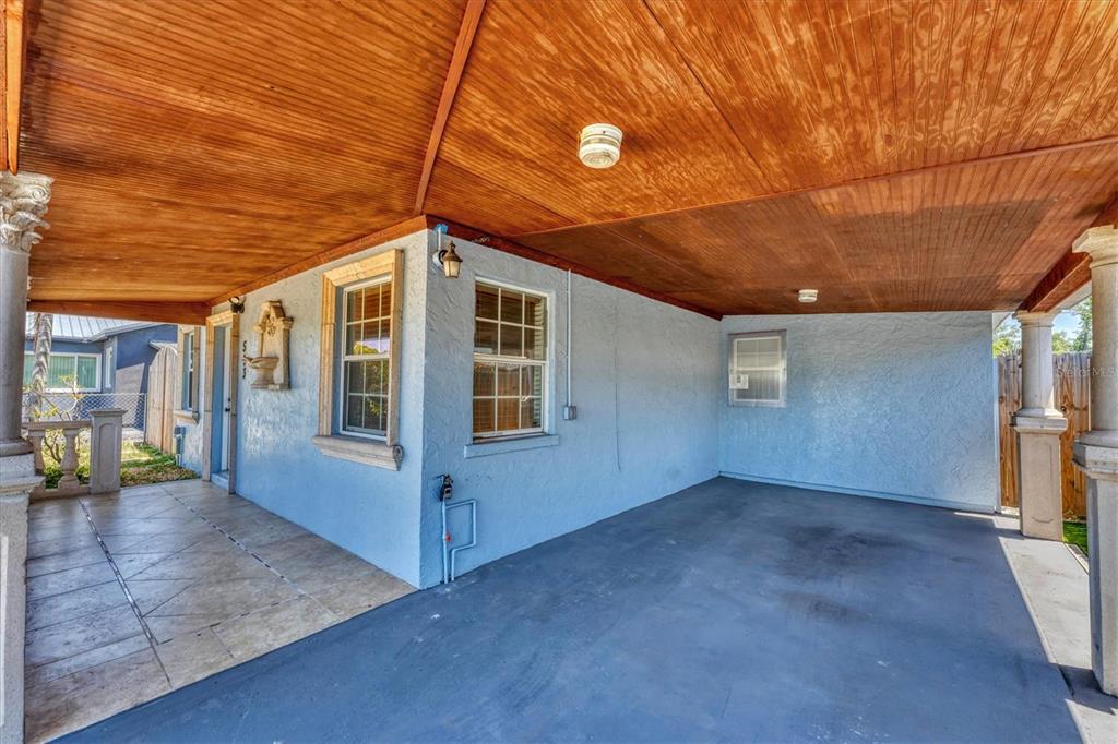 A covered porch and carport area with light blue stucco walls and a wood-paneled ceiling — 513 25TH AVENUE W, BRADENTON, FL