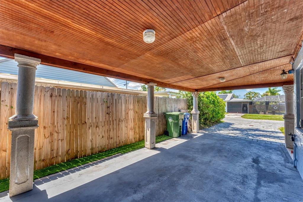 A covered carport features a wood-paneled ceiling, concrete flooring, and decorative stone-style pillars — 513 25TH AVENUE W, BRADENTON, FL