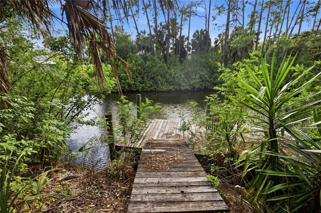 A wooden dock extends into a narrow canal surrounded by lush green trees and vegetation — 2091 CANNOLOT BOULEVARD, PORT CHARLOTTE, FL