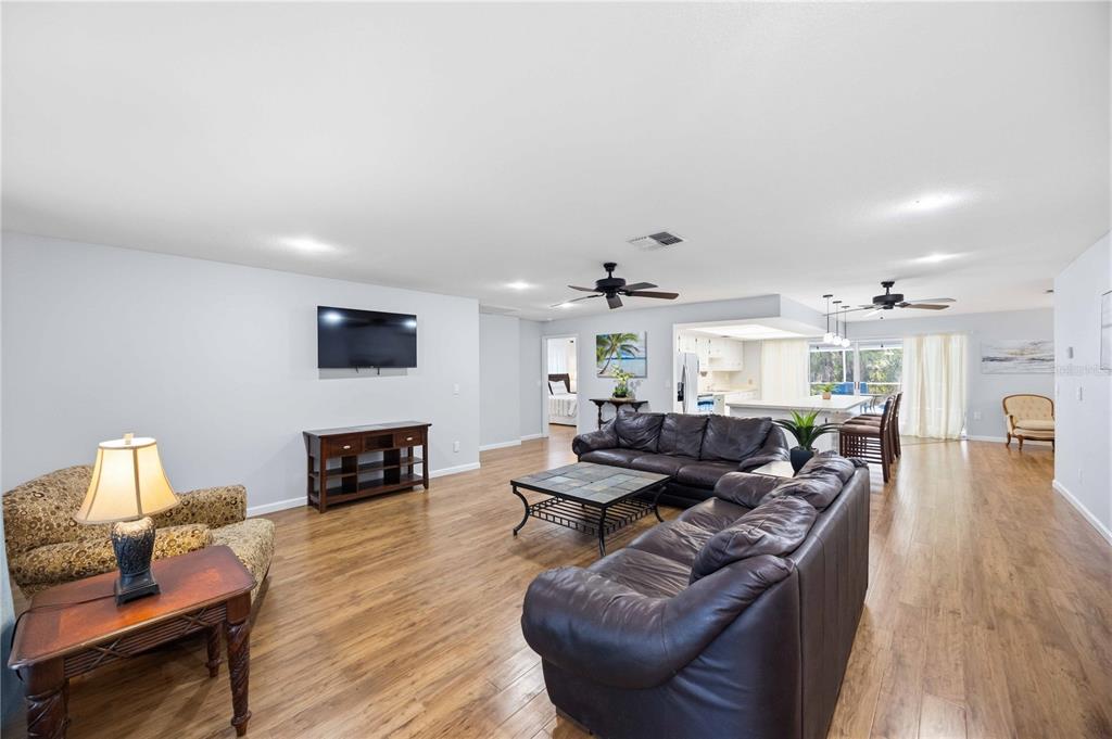 A spacious living room with wood-look flooring, leather sofas, and an open kitchen area — 2091 CANNOLOT BOULEVARD, PORT CHARLOTTE, FL
