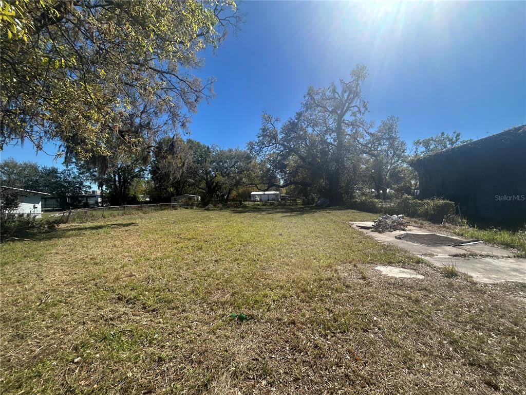 A grassy, vacant lot features a concrete slab and mature trees under a clear sky — 7707 GIBSONTON DRIVE, GIBSONTON, FL
