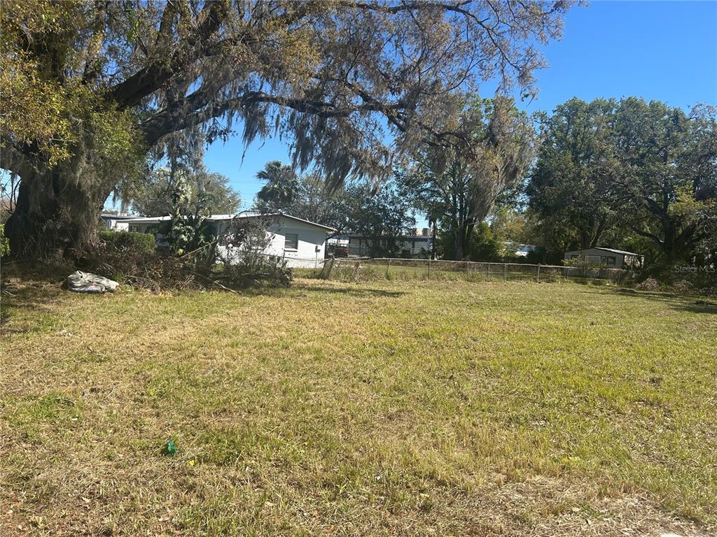 A grassy, vacant lot features a large oak tree and a chain-link fence — 7707 GIBSONTON DRIVE, GIBSONTON, FL