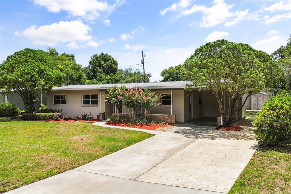 A single-story house with a concrete driveway, a carport, and landscaping under a blue sky — 5409 STRATEMEYER DRIVE, ORLANDO, FL