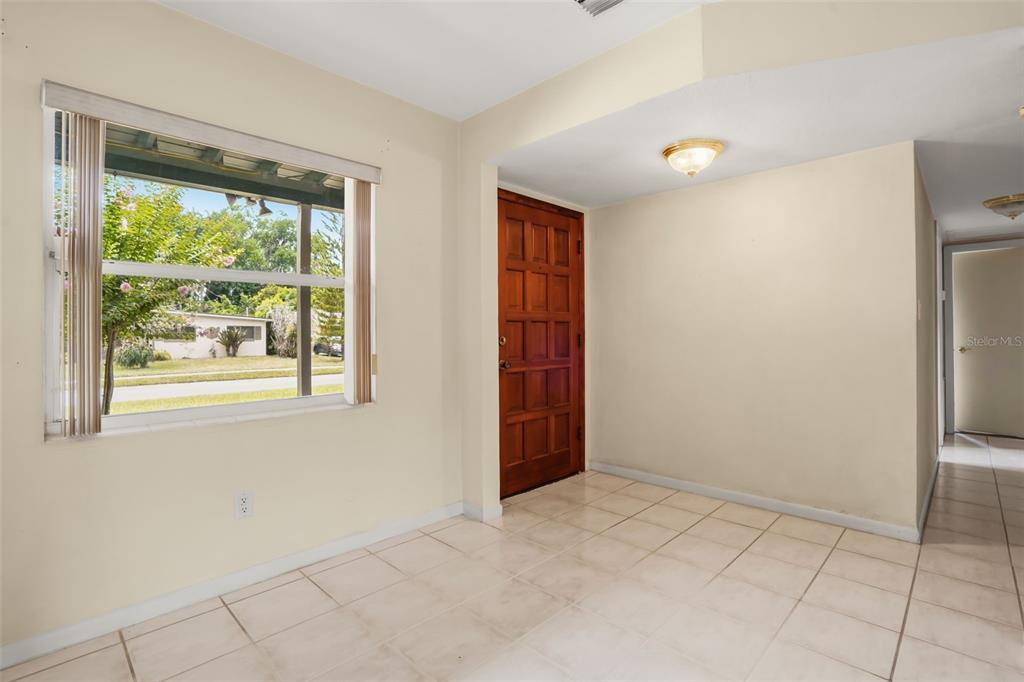 An empty room with light-colored tile flooring, a large window, and a wooden front door — 5409 STRATEMEYER DRIVE, ORLANDO, FL