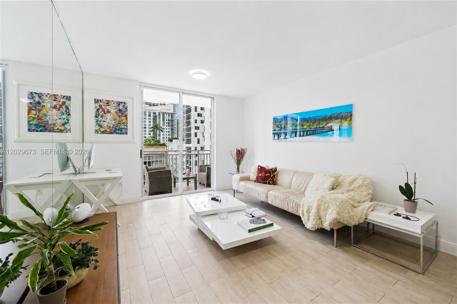 A bright living room features a white sofa, tiered coffee table, and a balcony view — 185 SE 14th Ter # 1410, Miami FL 33131, MIAMI, FL