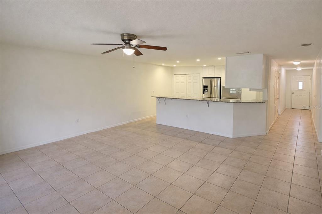 An open-concept living area features light-colored tile flooring, a ceiling fan, and a kitchen island — 627 BLUEBILL COURT, KISSIMMEE, FL