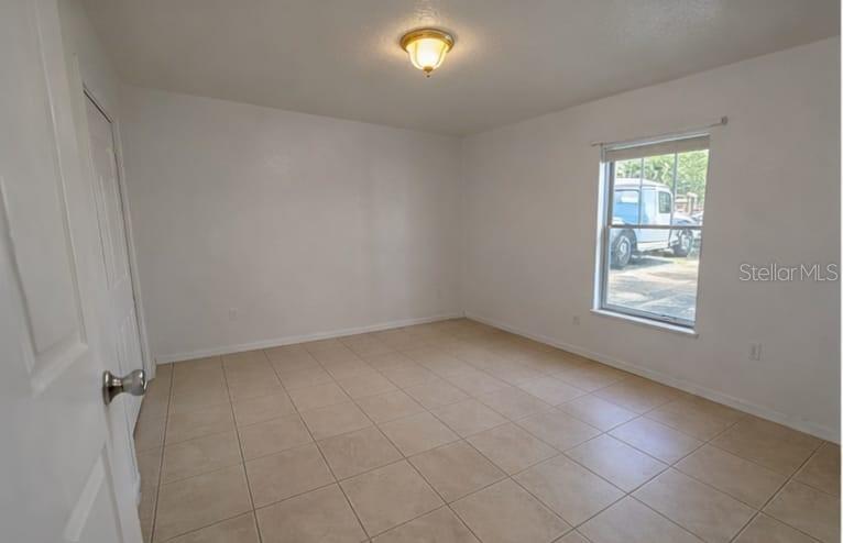 An empty bedroom features white walls, beige tile flooring, a ceiling light, and a window — 627 BLUEBILL COURT, KISSIMMEE, FL