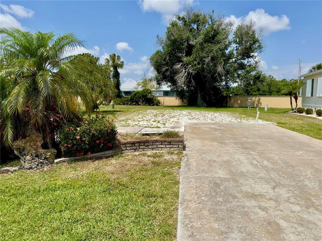 A concrete driveway leads to a sandy, undeveloped lot with trees and a brick planter — 2100 KINGS HIGHWAY UNIT 978, PORT CHARLOTTE, FL