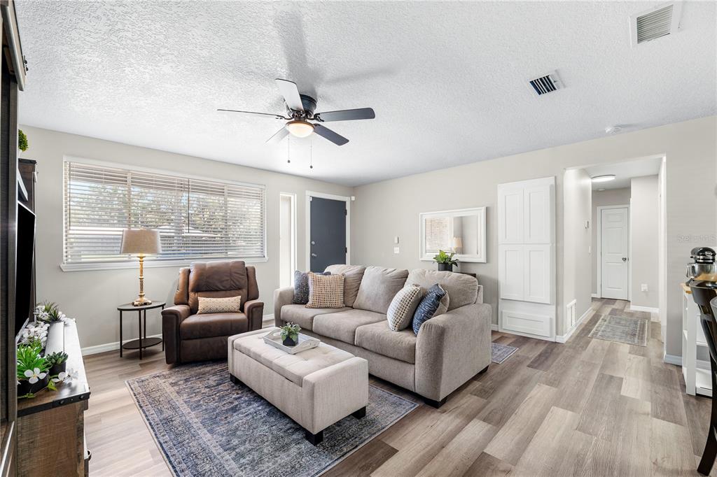 A living room features light wood-look flooring, a gray sofa, a brown recliner, and a ceiling fan — 1516 PROSPECT STREET, PALATKA, FL
