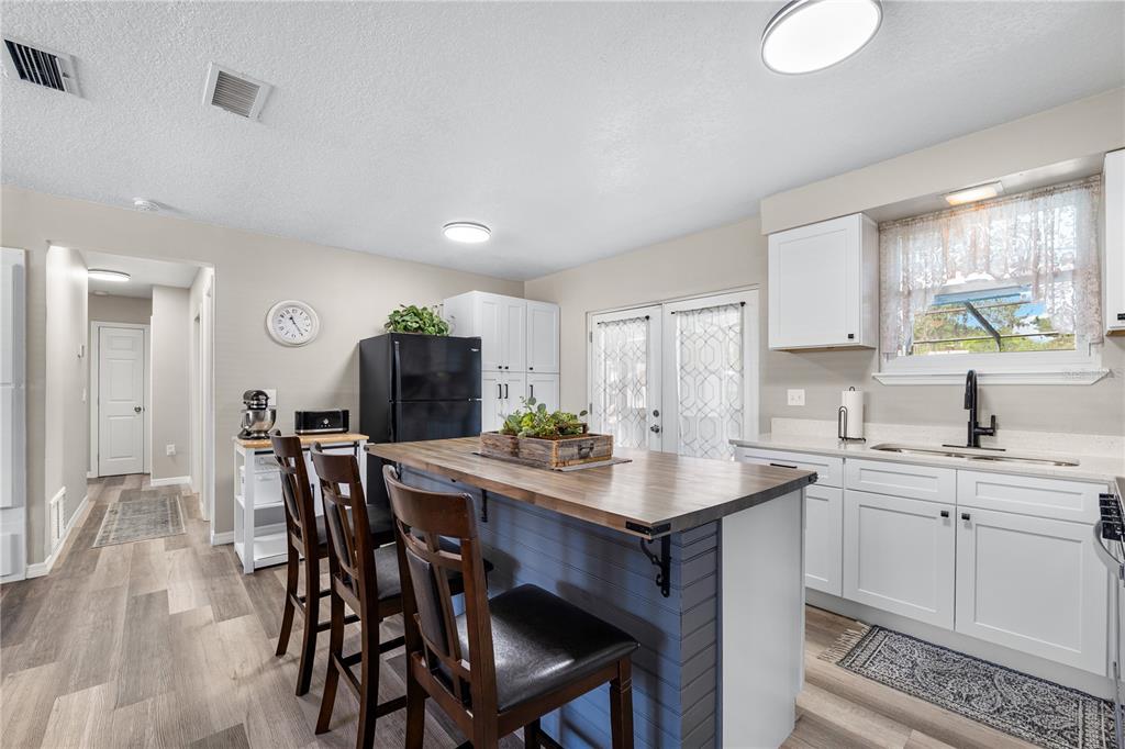 A kitchen features a wooden island with bar stools, white cabinetry, and light wood flooring — 1516 PROSPECT STREET, PALATKA, FL