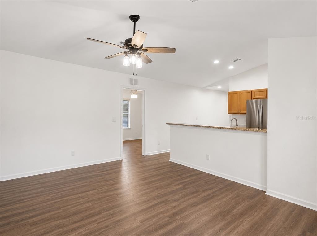 A living room with wood-look flooring and a ceiling fan opens to a kitchen area — 27349 ALOHA DRIVE, PUNTA GORDA, FL