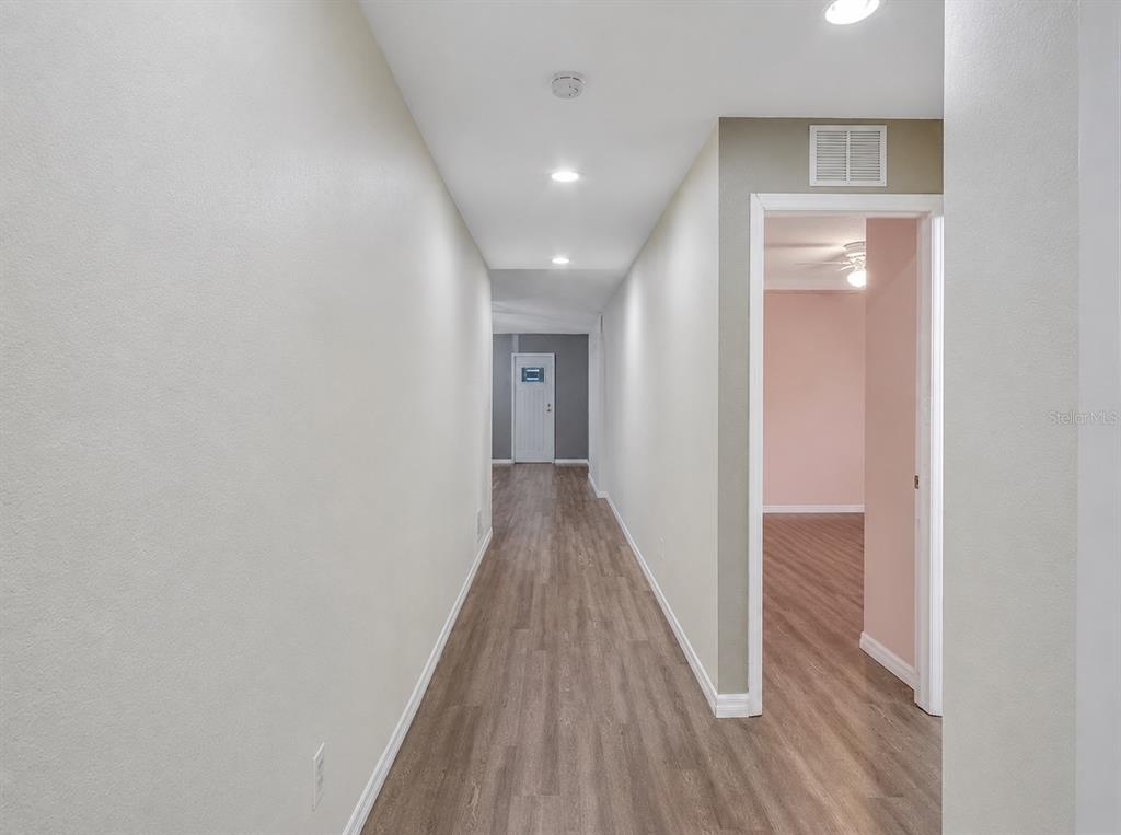 A hallway with light-colored walls and wood-look flooring leads to a doorway and room — 27349 ALOHA DRIVE, PUNTA GORDA, FL