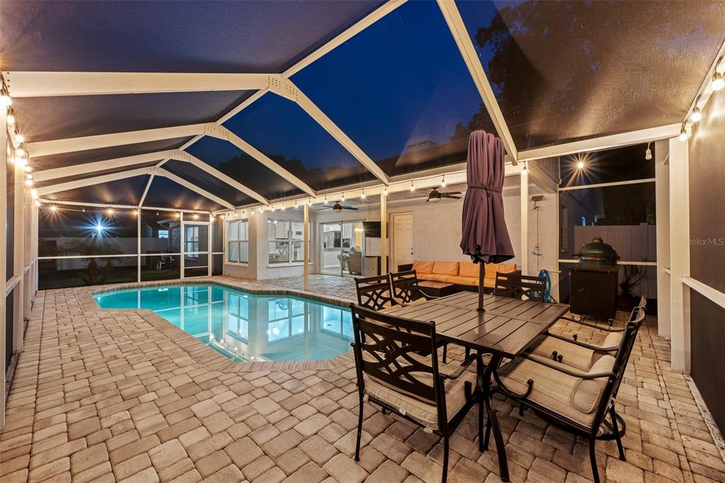 A screened-in patio features a swimming pool, outdoor dining set, and string lighting at night — 2410 ARBORWOOD DRIVE, VALRICO, FL