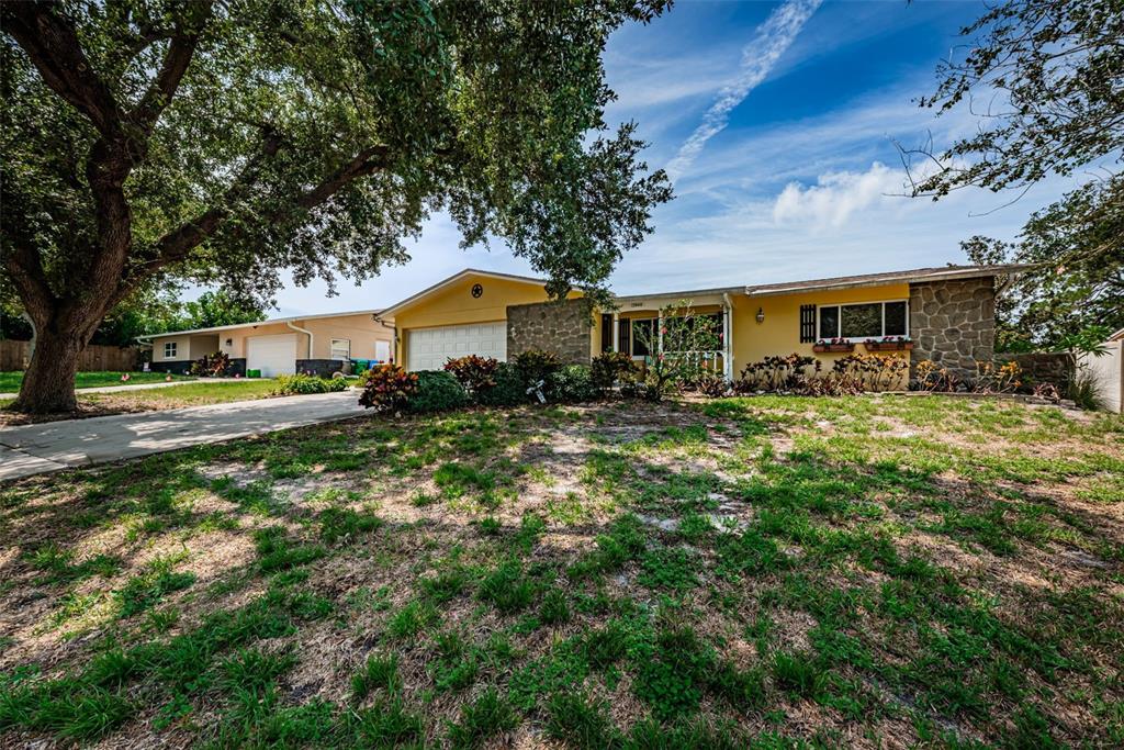 A yellow single-story house with a stone facade and a large tree in the yard — 13940 87TH AVENUE, SEMINOLE, FL