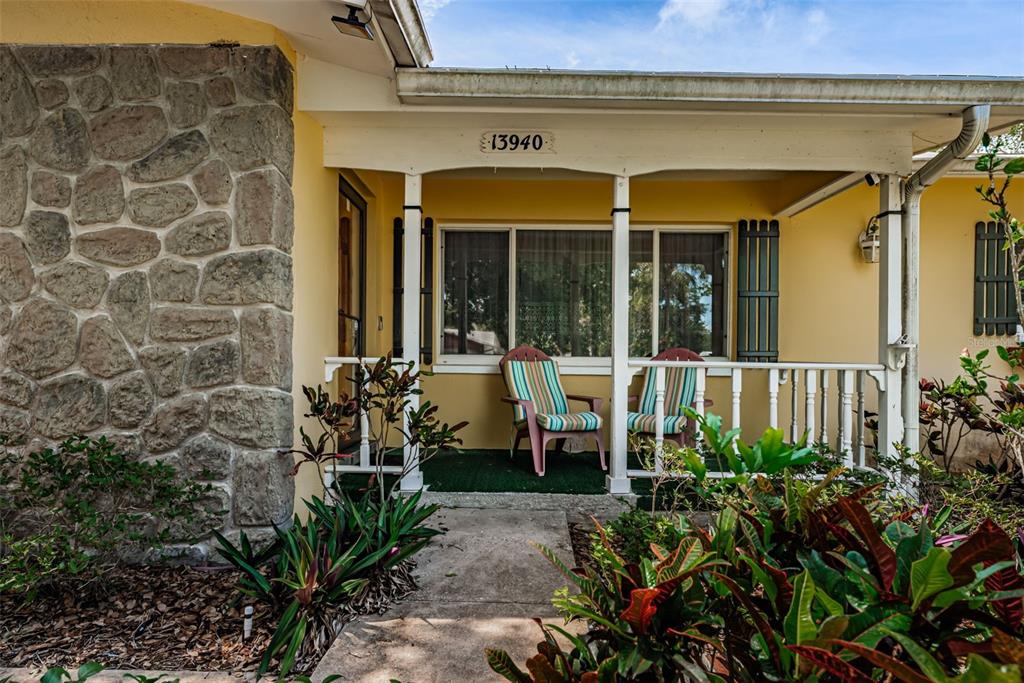 A stone-accented house exterior features a covered front porch with two chairs and landscaping — 13940 87TH AVENUE, SEMINOLE, FL
