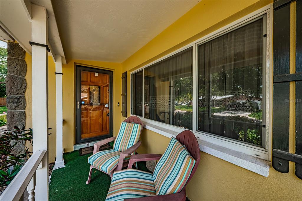 A covered porch features green outdoor carpeting, two striped chairs, and a wooden front door — 13940 87TH AVENUE, SEMINOLE, FL